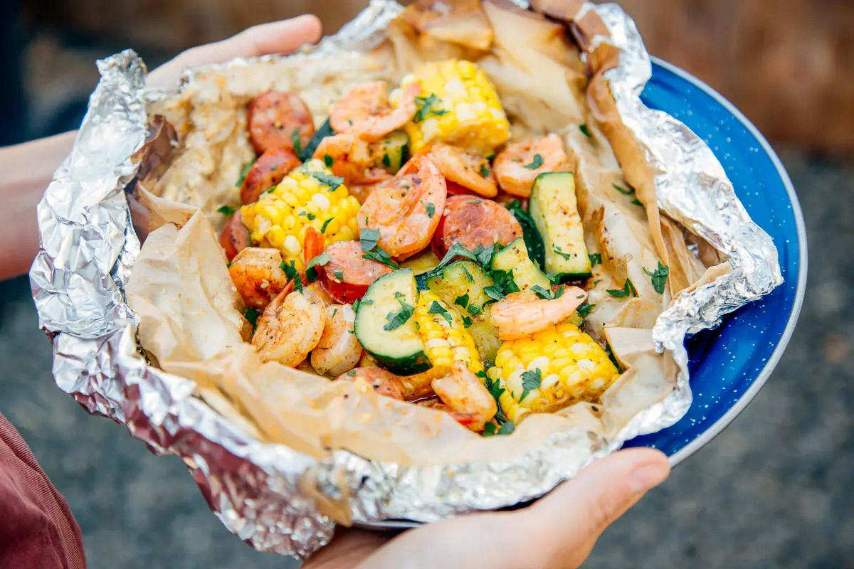A blue plate holds a foil packet of shrimp, sausage, corn and squash