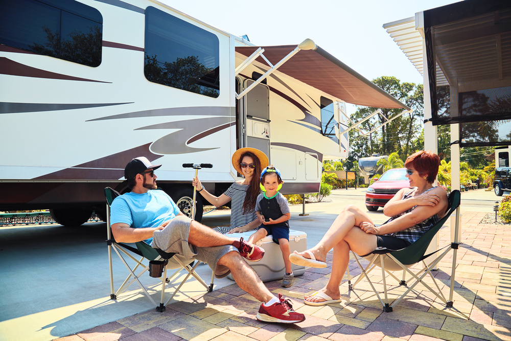 Mother, father, son and grandmother sittsng on chairs near camping trailer Full Time RV for Family Travel